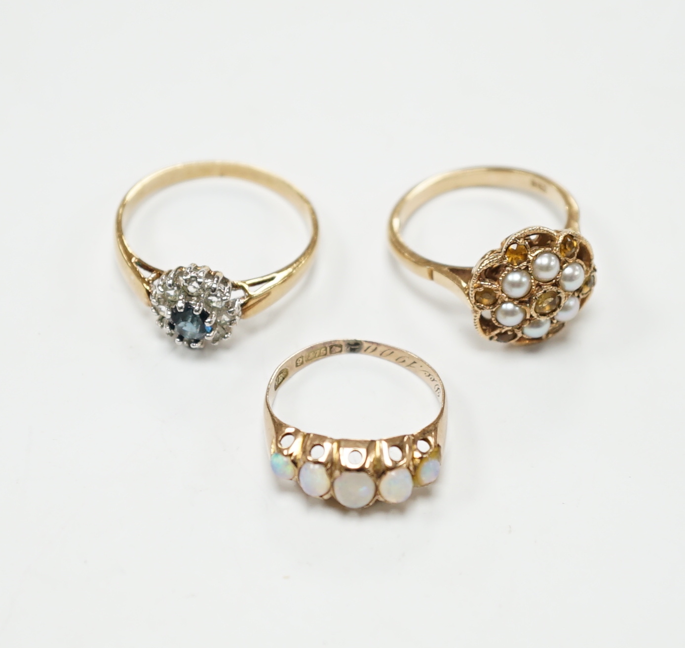 A late Victorian 9ct gold and graduated five stone opal set half hoop ring, size L, a 9ct, seed pearl and citrine cluster set flower head ring, gross 4.7 grams and a costume ring.